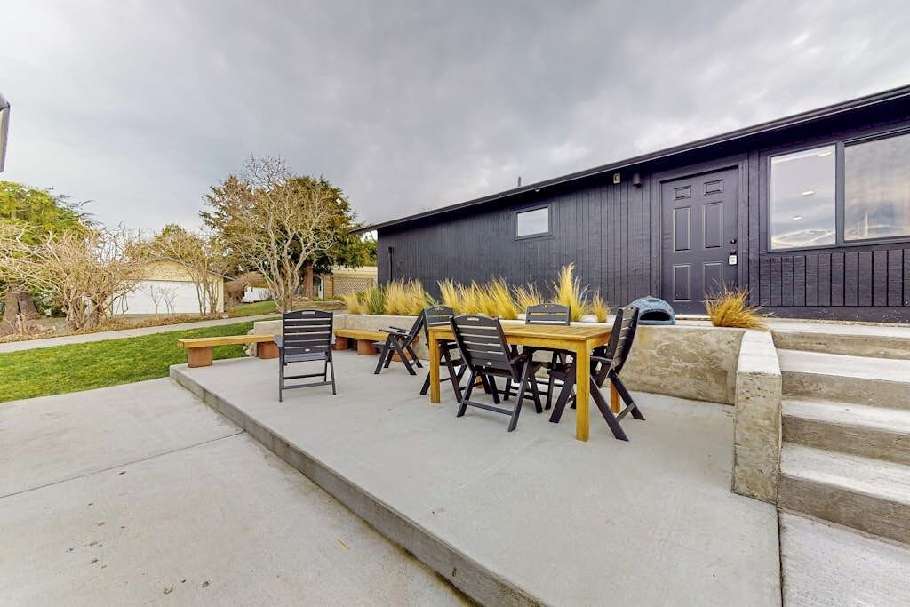 An outdoor patio with a table and chairs, a concrete pathway, and a dark building in the background.
