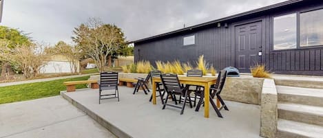 An outdoor patio with a table and chairs, a concrete pathway, and a dark building in the background.