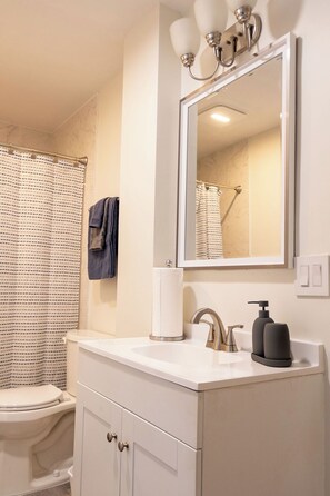Un bagno con un lavandino bianco, uno specchio illuminato, un porta asciugamani e un water.
