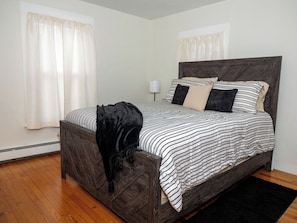 Una camera da letto con testiera in legno, un letto con biancheria a righe, una coperta nera e un tappeto nero.