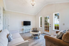 Ein Wohnzimmer mit Fernseher, einem weißen Sofa, einem braunen Sofa und einer Chandelier.