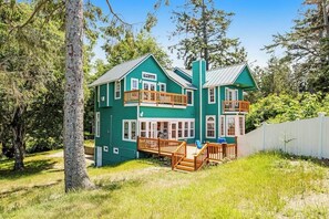 A two-story house with a balcony, surrounded by trees and a white fence. - Oceanfront 4 Bedroom Family Home with Private Beach Access and Fire Pit (Oak Harbor)