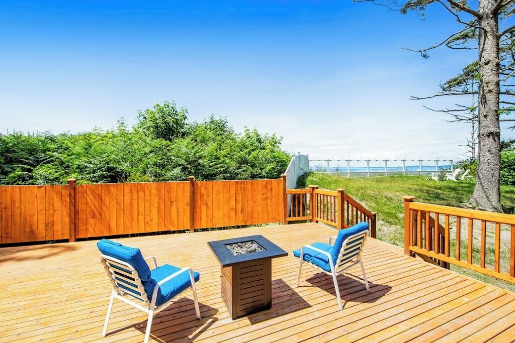 Una terraza de madera con dos sillas y una mesa, rodeada por una valla de madera y vistas al océano.