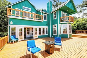 Ein zweistöckiges Haus mit einer Terrasse, Sitzgelegenheiten im Freien und einem Feuerkorb.