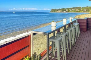 Eine Terrasse mit Meerblick, eine Reihe von Barhocker und ein rotes Geländer.