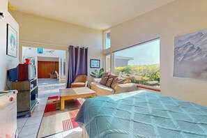 Ein Zimmer mit einem Bett, einem Sofa, einem Couchtisch, einem Fernseher und einem großen Fenster mit Blick auf Grünflächen.