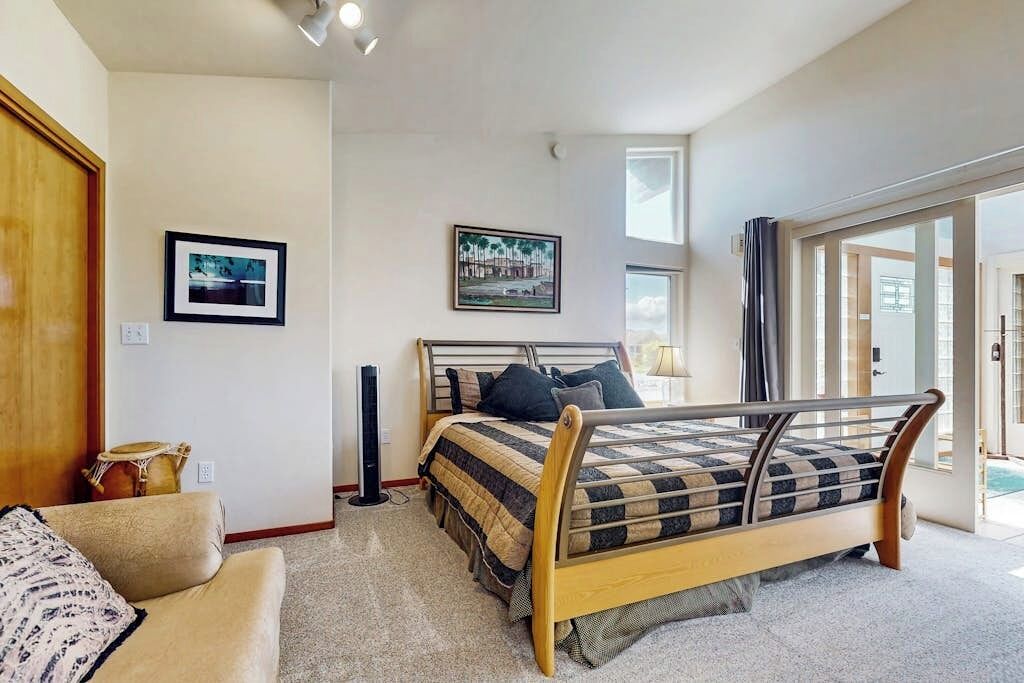 A bedroom with a bed, a couch, a standing heater, and a door leading to another room.