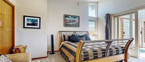 A bedroom with a bed, a couch, a standing heater, and a door leading to another room.
