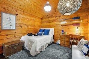 Habitación de cabaña de madera con una cama, un tocador, una silla y una lámpara en el techo.