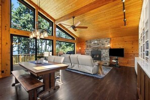 A spacious living area with a stone fireplace, a large window overlooking trees, and a ceiling fan.