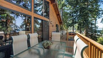 A wooden deck with a glass table and chairs, surrounded by trees.