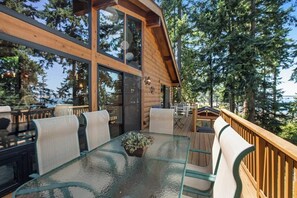 Una terraza de madera con una mesa y sillas de vidrio, rodeada de árboles.