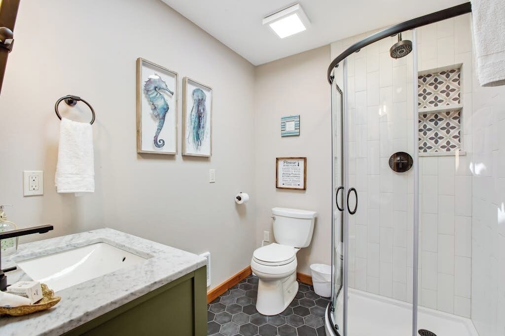A bathroom with a marble sink, a toilet, a glass shower enclosure, and framed artwork on the wall.