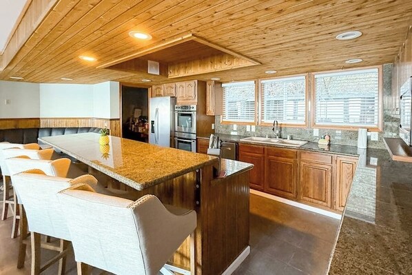 A modern kitchen with a central island, bar seating, wooden cabinetry, and large windows.