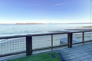 A waterfront view from a balcony with a metal railing, a grassy area, and a distant island.