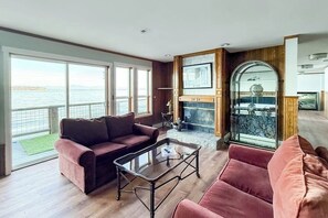 A spacious living area with a large window overlooking a body of water, a fireplace, and a glass-enclosed balcony.