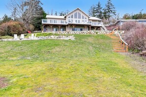 A two-story house with a stone retaining wall and a wooden staircase leading to a deck. - Stunning 4 Bedroom Beachfront Home in Greenbank with Panoramic Water Views (Greenbank)