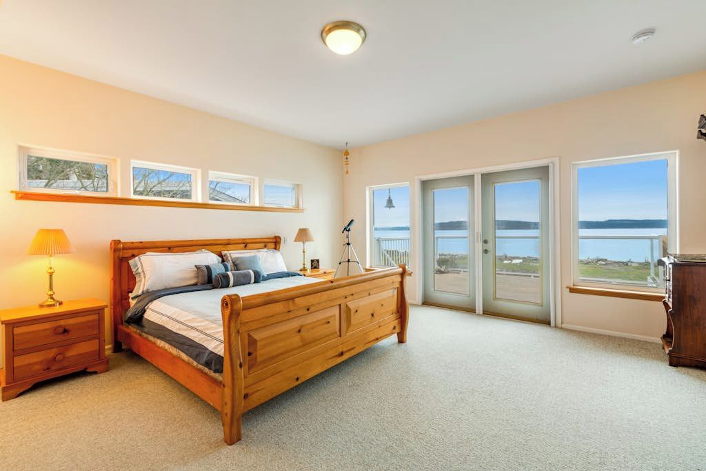 Een slaapkamer met een houten bed, een nachtkastje, een lamp en uitzicht op het omliggende landschap door grote ramen.