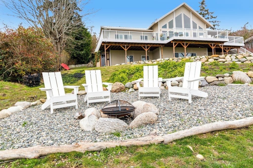 Une maison dotée d’une terrasse, entourée d’un espace recouvert de gravier, avec des chaises et un foyer.