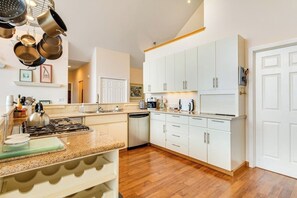 A kitchen with white cabinets, a stove, and hanging pots. - Stunning 4 Bedroom Beachfront Home in Greenbank with Panoramic Water Views (Greenbank)