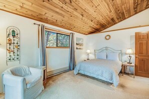 A bedroom with a wooden ceiling, a bed with two bedside tables, a chair, and a window with curtains. - Spectacular Waterfront Cabin in Eastsound with Private Deck and Mountain Views (Eastsound)