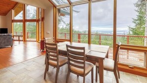 A dining area with a table and chairs, large windows, and a view of the outdoors. - Stunning Water View Retreat with Fireplace, Huge Deck, and Jetted Tub (Eastsound)