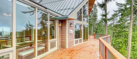 Moderni puinen terassi, jossa on lasiseinät ja joka sijaitsee metsän ympäröimänä.