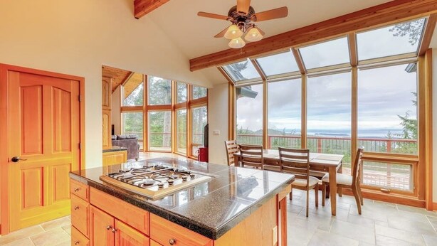 A kitchen with a large island, wooden cabinets, and a dining area with a view. - Stunning Water View Retreat with Fireplace, Huge Deck, and Jetted Tub (Eastsound)