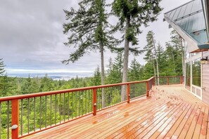 A wooden deck with a metal railing overlooking a forested area. - Stunning Water View Retreat with Fireplace, Huge Deck, and Jetted Tub (Eastsound)