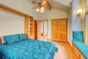 Una camera da letto con un letto, una ventola a soffitto, armadi in legno e una panca.