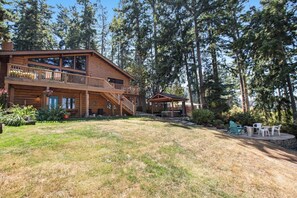 A two-story log cabin with a balcony, surrounded by a forest. - Scenic Waterfront Home with Hot Tub and Three Unique Living Spaces (Coupeville)