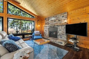 A cozy living room with a stone fireplace, a flat-screen TV, and a comfortable seating area. - Scenic Waterfront Home with Hot Tub and Three Unique Living Spaces (Coupeville)