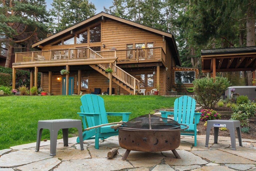 Une cabane en bois dotée d’un balcon, d’un espace salon extérieur et d’un foyer.