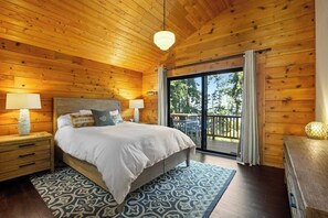 A wooden-paneled bedroom with a bed, nightstands, a patterned rug, and a view through a glass door. - Scenic Waterfront Home with Hot Tub and Three Unique Living Spaces (Coupeville)