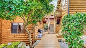Una cabaña de madera con una terraza de madera que conduce a una puerta, rodeada de árboles y follaje.