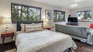 Un dormitorio con cama, sofá, televisión y ventanas amplias.