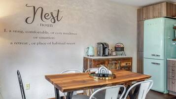 A dining area with a wooden table and metal chairs, a vintage-style refrigerator, and a wall with a definition of the word 'Nest.'