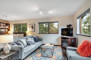 A living room with a sofa, coffee table, TV, bookshelf, and large windows. - Secluded Dog Friendly Studio with Hot Tub and Beach Access in Coupeville (Coupeville)