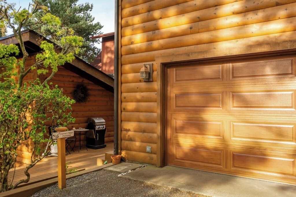 Une cabane en bois avec une porte de garage, un barbecue et un panneau indiquant une zone de stationnement.