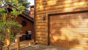 A wooden cabin with a garage door, a barbecue grill, and a sign indicating a parking area.
