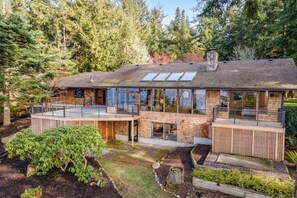 Een modern huis met twee verdiepingen en een groot terras, omringd door dicht bos.