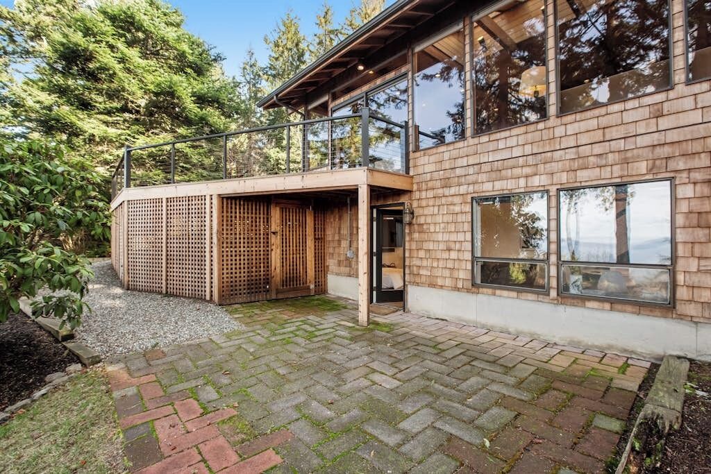A modern house with a brick exterior, a wooden deck, and a glass door leading to a covered outdoor area.