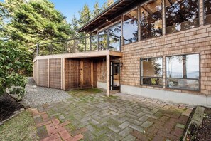 Een modern huis met een bakstenen gevel, een houten terras en een glazen deur naar een overdekt buitengebied.