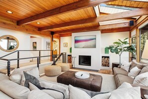 A spacious living room with a high ceiling, a fireplace, a staircase, and a large window. - Exquisite Oceanfront Home with Balcony, and Gym in Freeland (Freeland)