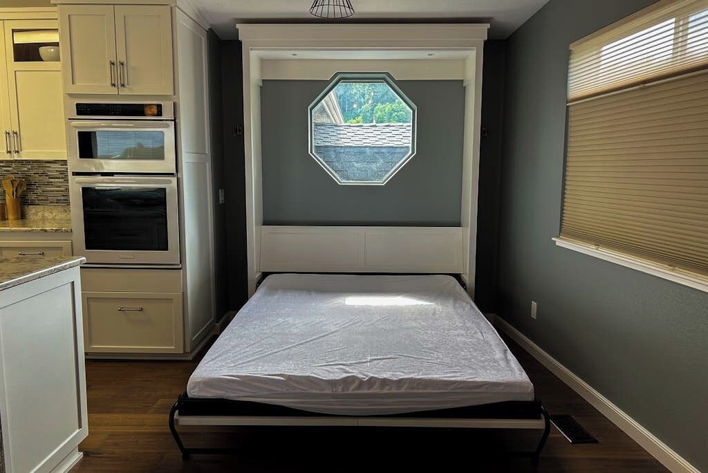 A bedroom with a bed, built-in cabinetry, an oven, and a window with a view.