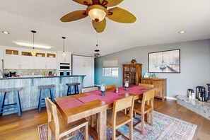 Een ruime keuken met een centraal kookeiland, houten barkrukken en een eethoek met een grote tafel.