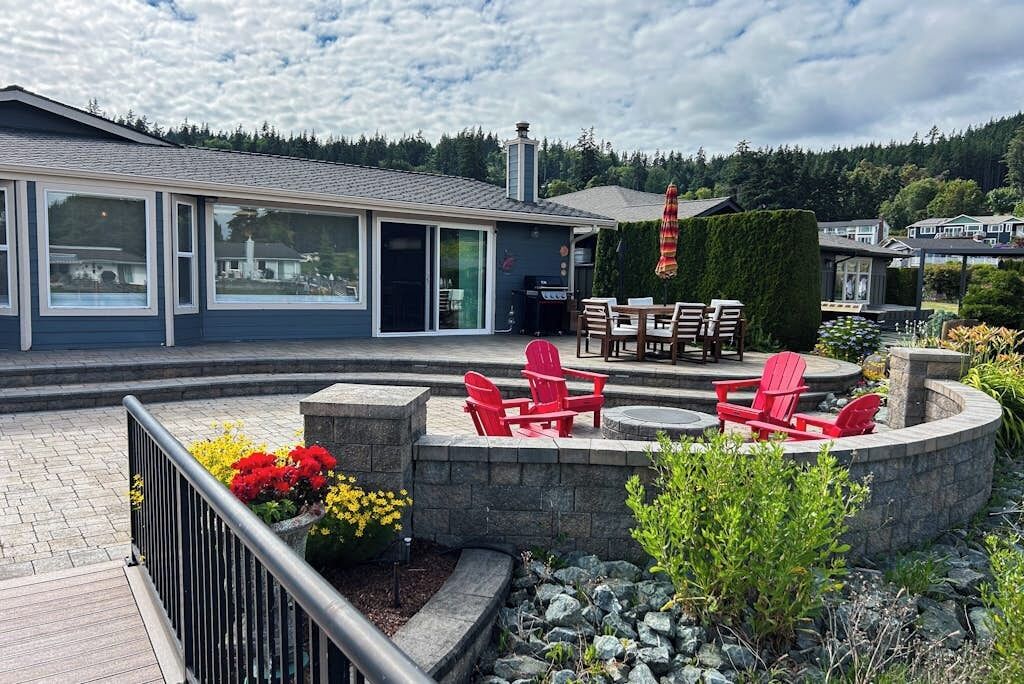 Ein modernes Gebäude mit einer Terrassenanlage, die rote Adirondack-Stühle und einen Tisch zeigt, umgeben von einer Steinschranke und Kübelpflanzen.