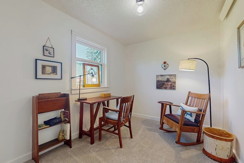 Une pièce avec une table et des chaises en bois, une fenêtre avec des stores, un lampadaire et une étagère ornée d’objets décoratifs.