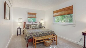 Une chambre à coucher avec un lit, deux tables de chevet, un banc et une fenêtre avec des stores.
