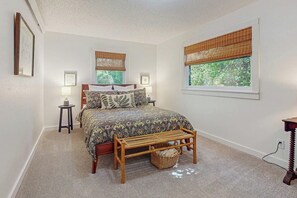 A bedroom with a bed, two bedside tables, a bench, and a window with blinds.